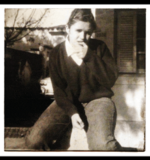 a black and white photo of a young man smoking a cigarette in front of a building that has the number 5 on it