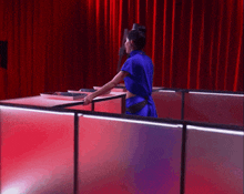 a woman in a blue shirt is standing in front of a red curtain behind a counter