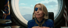 a woman wearing a blue eye patch looks out of a window