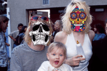 a man with a skull on his face holds a baby and a woman with a skull on her face holds a bottle