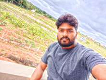 a man with a beard is taking a selfie with a field in the background