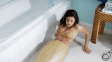 a woman in a mermaid costume laying on the floor next to a bathtub