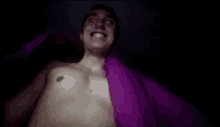 a man without a shirt is laying in bed with a purple blanket .