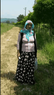 a woman wearing a floral skirt and a scarf stands in a field