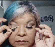 a woman with blue hair is applying makeup to her eyes