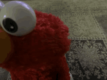 elmo is sitting on a rug and looking at the camera