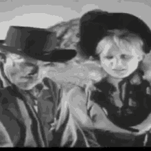 a man and a boy in cowboy hats are standing next to each other in a black and white photo .