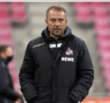 a man wearing a rewe jacket stands in front of a pink stadium