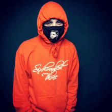 a man wearing a mask and an orange hoodie that says sightings of three