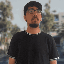 a man wearing glasses and a black shirt stands in front of trees