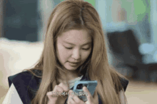 a woman with blonde hair is looking at a cell phone with korean writing on it