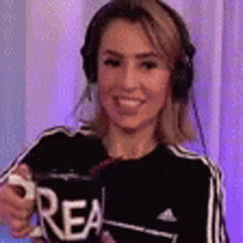 a woman wearing headphones and a black shirt is pointing at the camera and smiling .