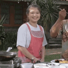 a woman in an apron is standing in front of a table with bowls of food and a stove .