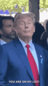 donald trump is wearing a blue suit and red tie and is standing in front of a crowd .