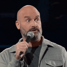 a bald man with a beard is holding a microphone and making a funny face