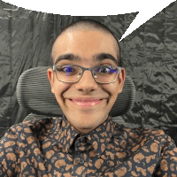 a young man wearing glasses and a paisley shirt is smiling while sitting in an office chair .