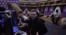 a man sitting in a locker room with purple shirts hanging on the wall with the number 20 on them