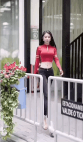 a woman in a red crop top and black pants is walking across a fence .