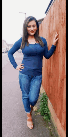 a woman in a blue shirt and jeans leans against a red fence