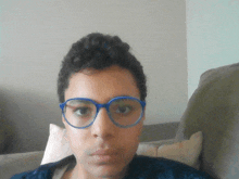 a young man wearing blue glasses looks at the camera