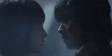 a man and a woman are looking into each other 's eyes in a dark room .
