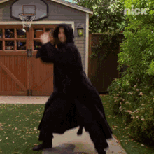 a man in a black robe is standing in front of a garage door with a basketball hoop on the wall above him