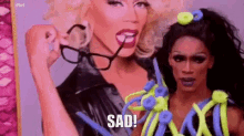 a drag queen is holding a pair of glasses in front of another drag queen .