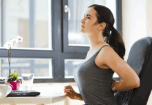 a woman stretches her back while sitting at a desk with a laptop on it