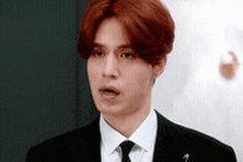 a young man with red hair is wearing a suit and tie and making a funny face .