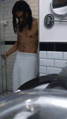 a shirtless man with long hair is wrapped in a towel in a bathroom .