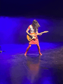 a woman in a red and white polka dot dress is playing a guitar