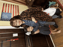 a woman in a leopard print jacket holds a little girl in front of an american flag