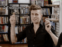 a man in a black shirt is standing in front of a bookshelf with the word treasure written above him