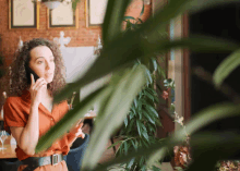 a woman with curly hair is talking on a cell phone in front of a plant