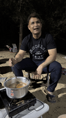 a man wearing a brooklyn t-shirt sits on a stool