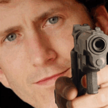 a man is pointing a gun at the camera while wearing a black shirt .