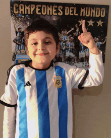 a young boy giving a thumbs up in front of a poster that reads campeones del mundo