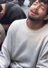 a man with a beard wearing a white sweater with xhk on the sleeve