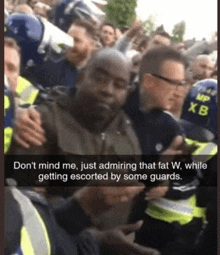 a man in a crowd is being escorted by a police officer wearing a helmet that says " mp xb "