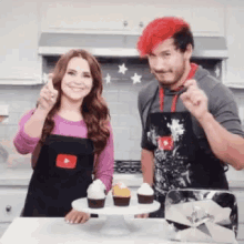 a man and a woman are standing next to each other in a kitchen with cupcakes on a cake stand .