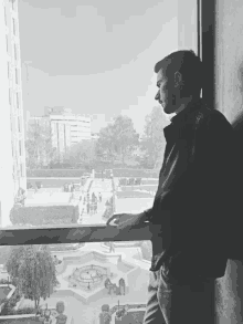 a man leans against a wall looking out a window at a park