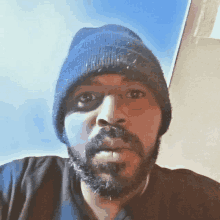 a man with a beard wearing a blue beanie looks at the camera