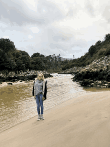 a woman standing on a sandy beach near a river