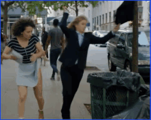 a woman in a suit and a woman in a skirt are running down a sidewalk .