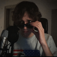 a young man wearing sunglasses and a gray shirt with an american flag on it