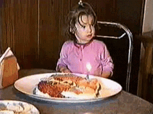 a little girl is sitting at a table with a plate of food and a candle in her mouth .