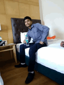 a man sits on a bed with a bottle of water in his hand