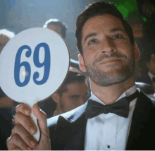 a man in a tuxedo is holding up a sign that says 69