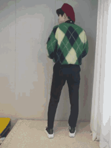 a man wearing a plaid sweater and black pants is standing on a rug