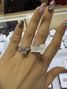 a woman is wearing a diamond ring with a tag that says ' emerald cut ' on it